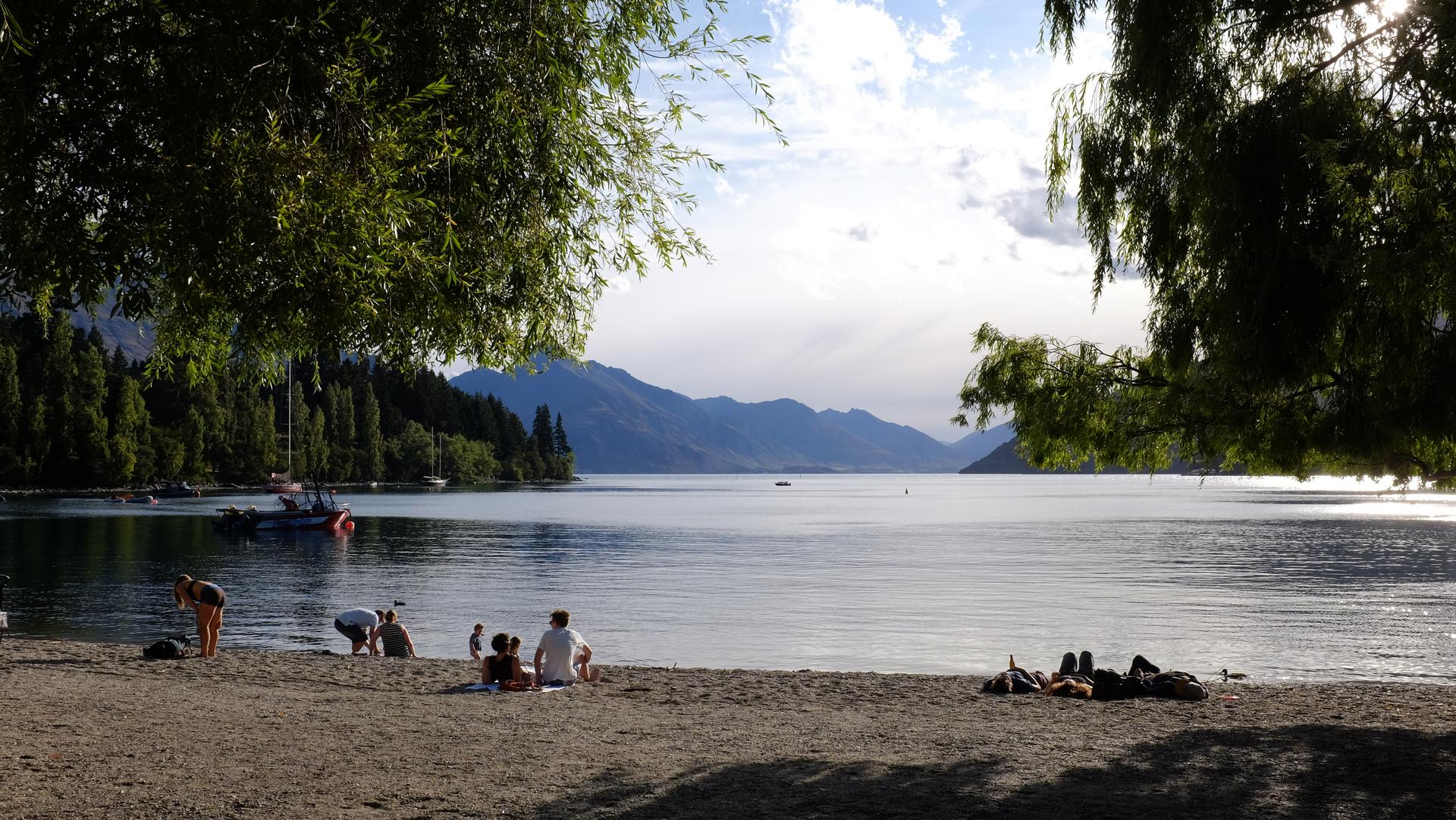 Queenstown beach with people lounging in the sand and mountains in the distance.